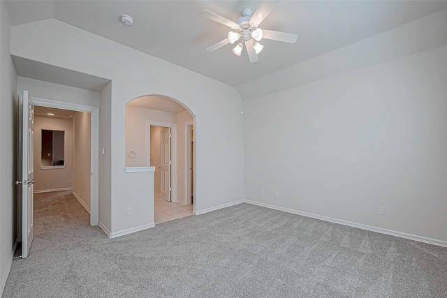 empty room featuring a ceiling fan, light colored carpet, arched walkways, and baseboards