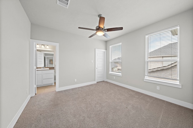 unfurnished bedroom with ensuite bathroom, sink, light carpet, and ceiling fan