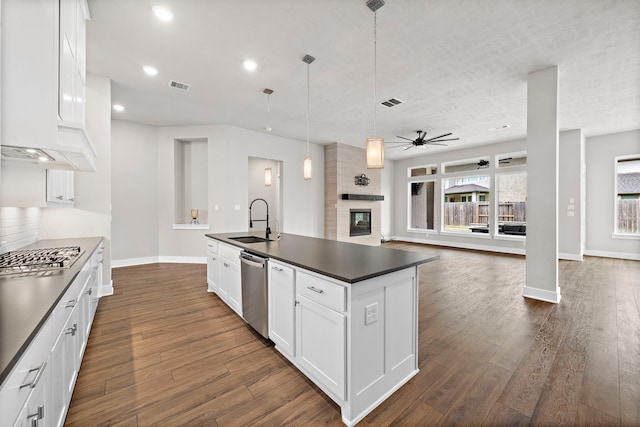 kitchen featuring pendant lighting, sink, appliances with stainless steel finishes, white cabinets, and a center island with sink