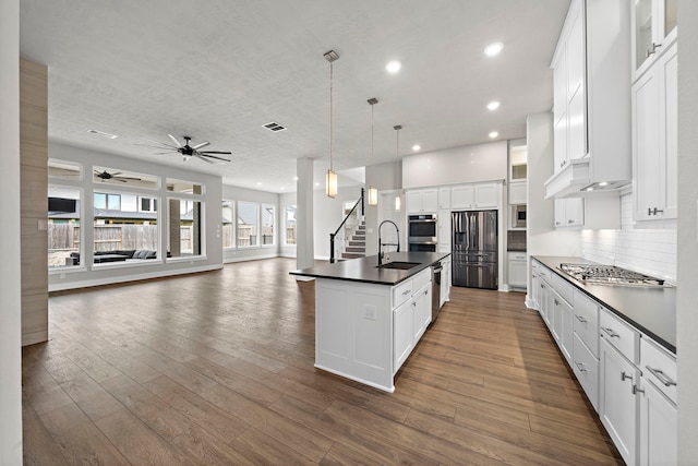 kitchen with hanging light fixtures, an island with sink, white cabinets, and appliances with stainless steel finishes