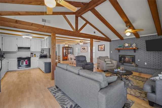 living room featuring a fireplace, light hardwood / wood-style floors, vaulted ceiling with beams, ceiling fan, and brick wall