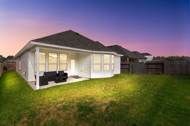 back house at dusk featuring an outdoor living space, a patio area, and a lawn