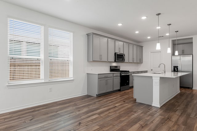 kitchen with decorative light fixtures, stainless steel appliances, dark hardwood / wood-style flooring, gray cabinets, and an island with sink