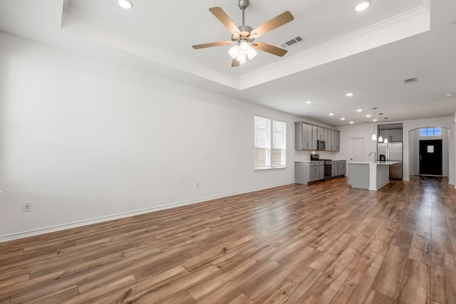 unfurnished living room featuring ceiling fan, ornamental molding, wood-type flooring, and a tray ceiling