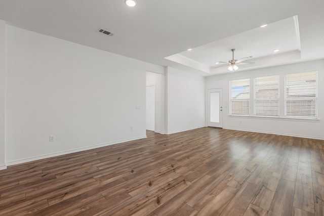 unfurnished living room featuring a tray ceiling, ceiling fan, and dark hardwood / wood-style floors