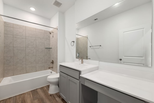 full bathroom featuring wood-type flooring, toilet, tiled shower / bath combo, and vanity