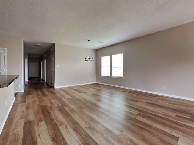 unfurnished living room featuring a notable chandelier, a textured ceiling, and hardwood / wood-style flooring