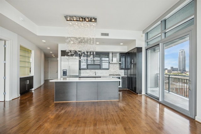 kitchen featuring backsplash, built in fridge, wall chimney exhaust hood, and dark wood-type flooring