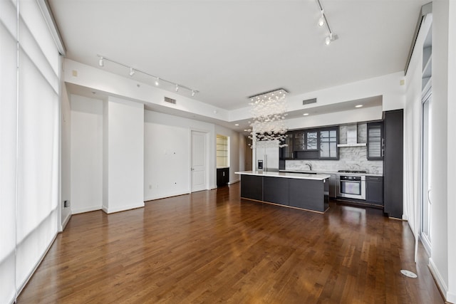 kitchen with decorative backsplash, appliances with stainless steel finishes, wall chimney range hood, a center island, and dark hardwood / wood-style floors