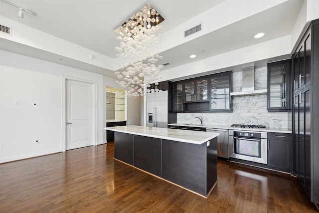 kitchen with appliances with stainless steel finishes, dark wood-type flooring, sink, wall chimney range hood, and a kitchen island