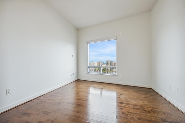 spare room featuring baseboards, a city view, and wood finished floors