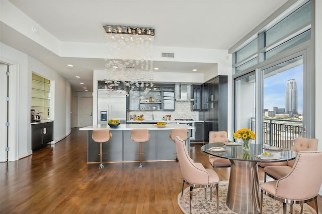 kitchen featuring wall chimney range hood, dark hardwood / wood-style floors, backsplash, a breakfast bar area, and stainless steel built in fridge