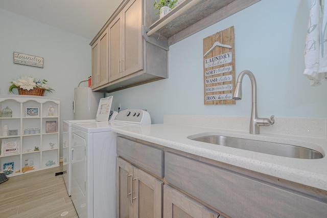 washroom featuring a sink, light wood-style floors, water heater, cabinet space, and washer and clothes dryer