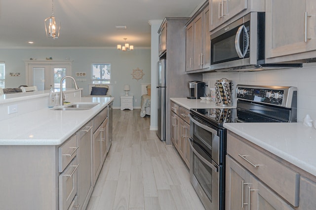 kitchen with an inviting chandelier, decorative light fixtures, ornamental molding, stainless steel appliances, and sink