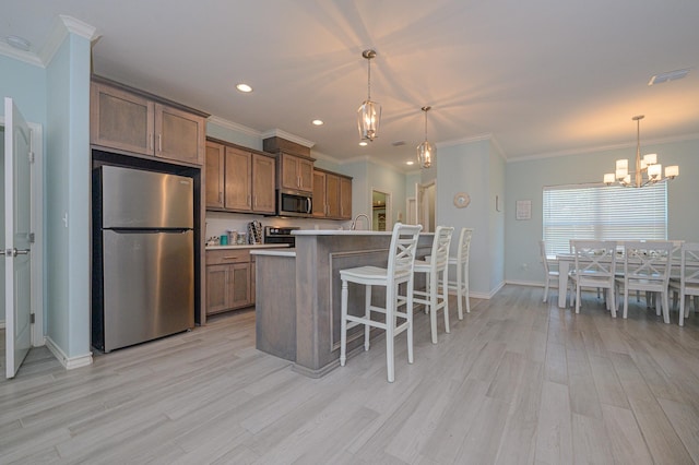 kitchen with light wood finished floors, a center island with sink, appliances with stainless steel finishes, light countertops, and pendant lighting