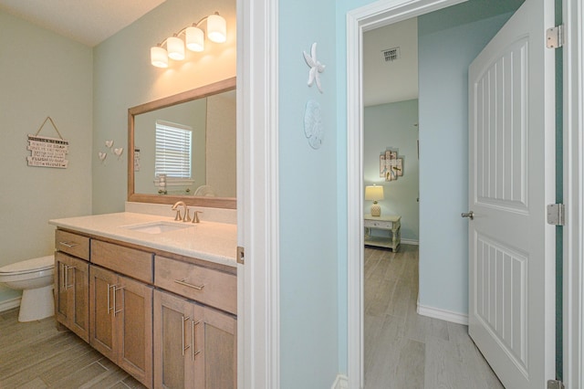 bathroom featuring toilet, wood finished floors, vanity, visible vents, and baseboards