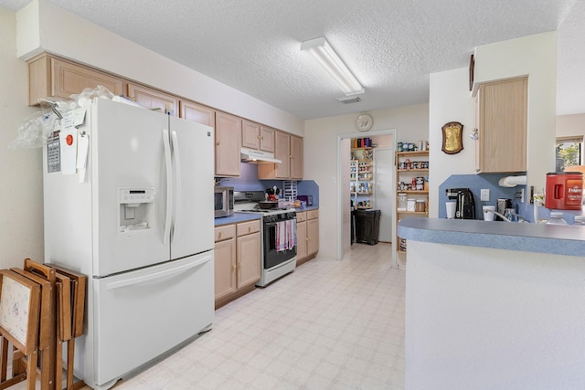 kitchen with light brown cabinetry, white appliances, and a textured ceiling