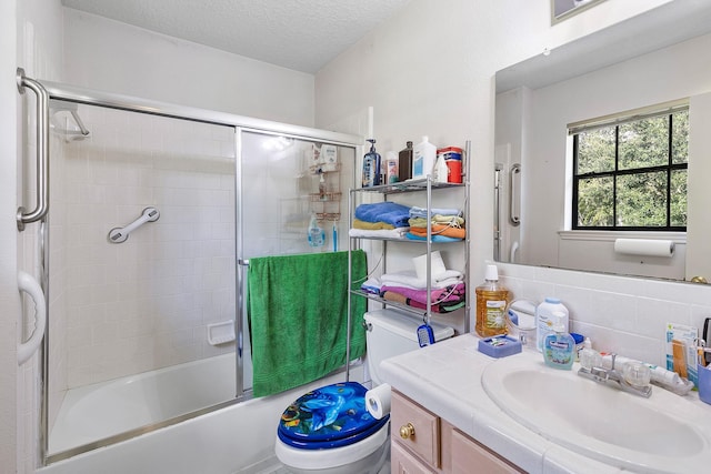 full bathroom featuring vanity, bath / shower combo with glass door, toilet, and a textured ceiling