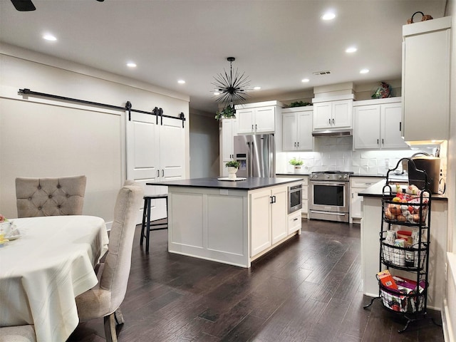 kitchen featuring dark countertops, a barn door, stainless steel appliances, and backsplash