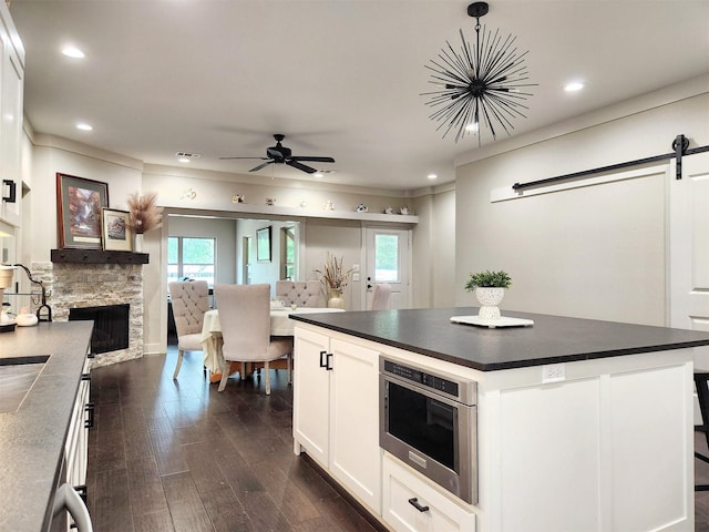 kitchen featuring dark countertops, a barn door, dark wood-type flooring, and a stone fireplace