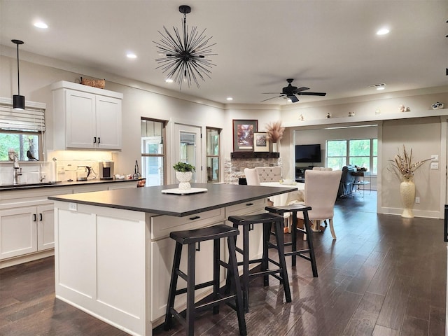 kitchen with dark wood-style floors, a center island, dark countertops, backsplash, and a sink