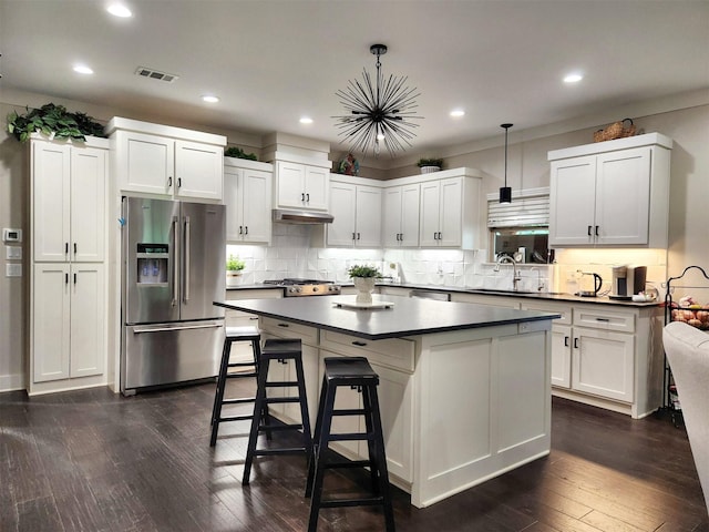 kitchen with visible vents, dark countertops, under cabinet range hood, stainless steel refrigerator with ice dispenser, and a sink