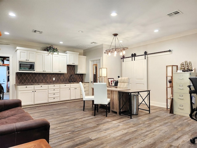 kitchen featuring light wood finished floors, a barn door, visible vents, decorative backsplash, and stainless steel microwave