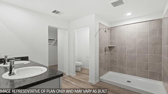 bathroom featuring a tile shower, hardwood / wood-style floors, vanity, and toilet