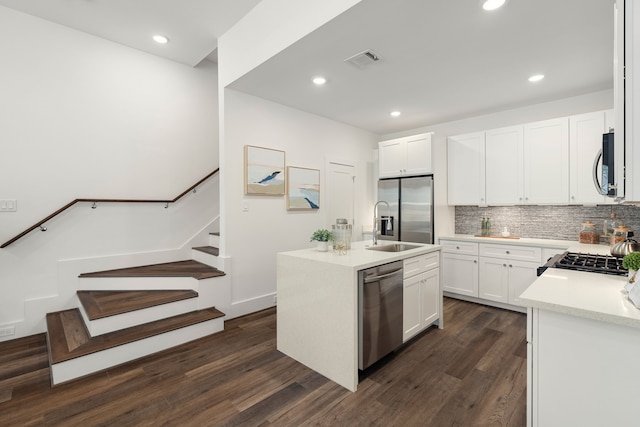 kitchen with dark wood-style flooring, a center island with sink, stainless steel appliances, tasteful backsplash, and visible vents