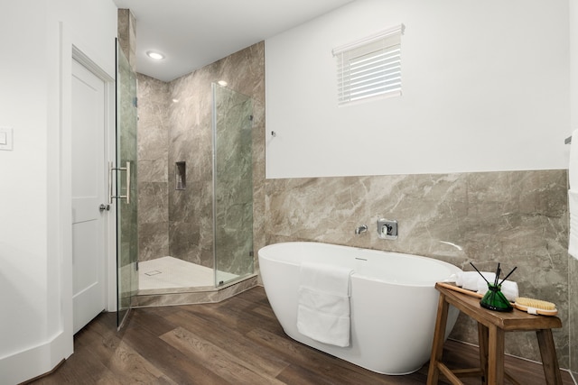 full bath with a stall shower, a freestanding bath, tile walls, and wood finished floors