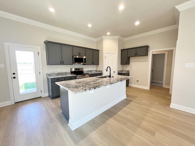 kitchen featuring light stone countertops, a kitchen island with sink, stainless steel appliances, a sink, and crown molding