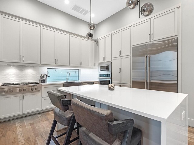 kitchen featuring decorative backsplash, built in appliances, sink, light hardwood / wood-style floors, and a center island