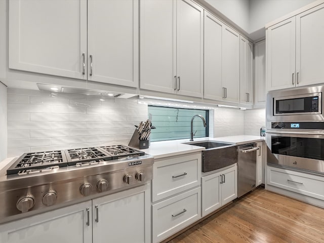 kitchen with light wood-type flooring, appliances with stainless steel finishes, backsplash, white cabinets, and sink