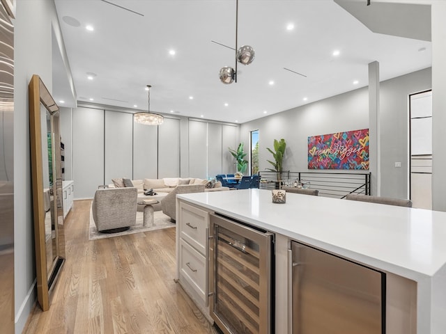 kitchen with light wood-type flooring, wine cooler, white cabinetry, a center island, and decorative light fixtures