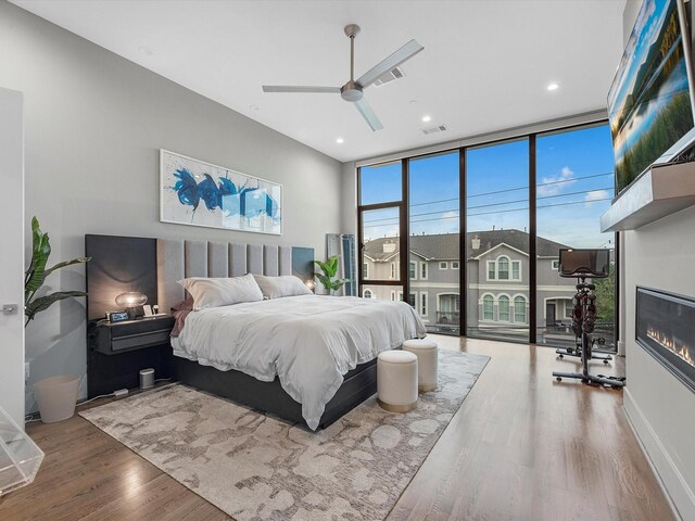 bedroom featuring ceiling fan, expansive windows, and hardwood / wood-style floors