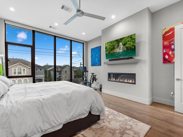 bedroom with ceiling fan, expansive windows, hardwood / wood-style flooring, and access to exterior