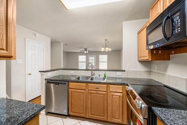 kitchen with light tile patterned floors, appliances with stainless steel finishes, dark stone countertops, ceiling fan with notable chandelier, and sink