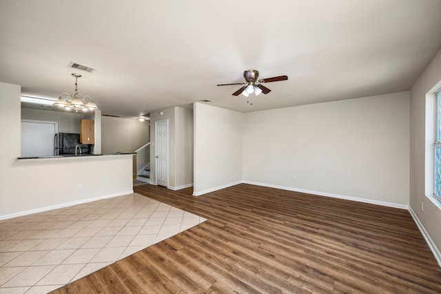 unfurnished living room with light tile patterned flooring and ceiling fan with notable chandelier