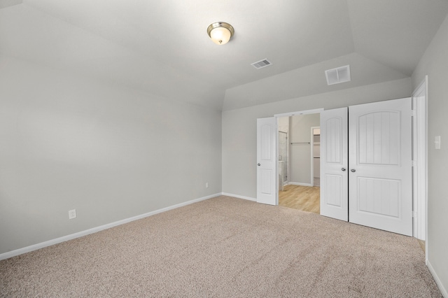 unfurnished bedroom with a closet, a spacious closet, vaulted ceiling, and light colored carpet