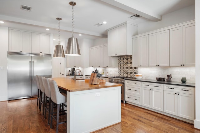 kitchen with high end appliances, decorative light fixtures, hardwood / wood-style flooring, white cabinets, and an island with sink