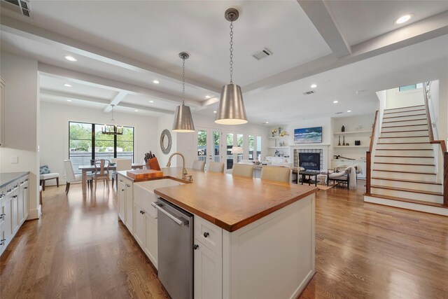 kitchen with dishwasher, light hardwood / wood-style flooring, beamed ceiling, a center island with sink, and white cabinets