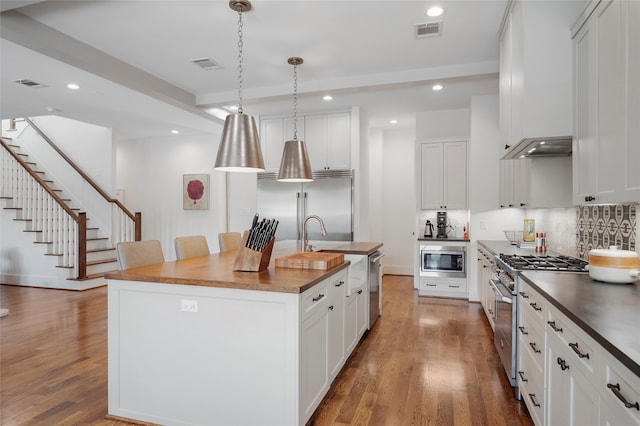 kitchen featuring built in appliances, white cabinets, hardwood / wood-style floors, and a center island with sink