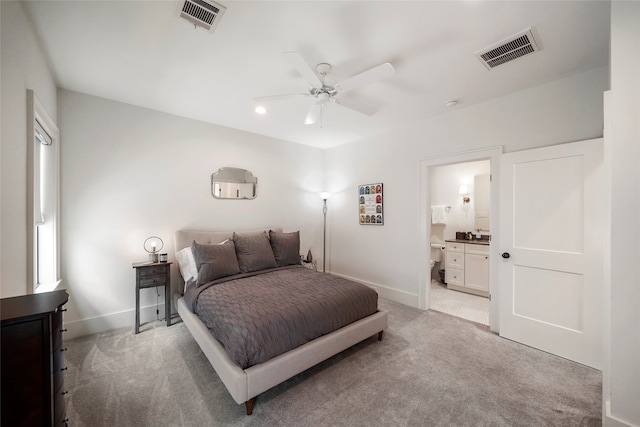 bedroom with ceiling fan, light colored carpet, and ensuite bath