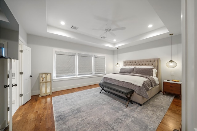 bedroom with wood-type flooring, a tray ceiling, and ceiling fan