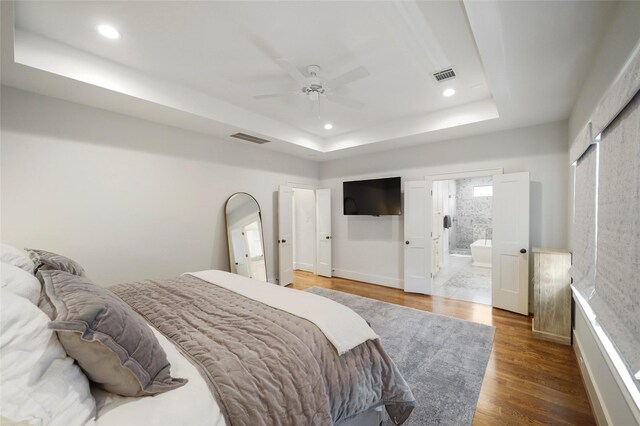 bedroom featuring a tray ceiling, ceiling fan, dark hardwood / wood-style flooring, and ensuite bathroom