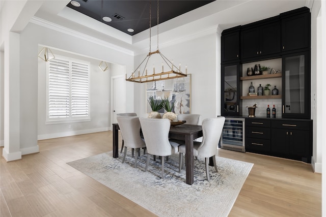 dining area with a raised ceiling, bar, beverage cooler, crown molding, and light hardwood / wood-style floors