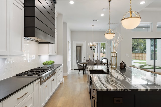 kitchen with sink, dark stone countertops, decorative light fixtures, backsplash, and a spacious island