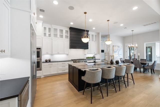 kitchen with white cabinets, light hardwood / wood-style floors, a center island with sink, and decorative light fixtures