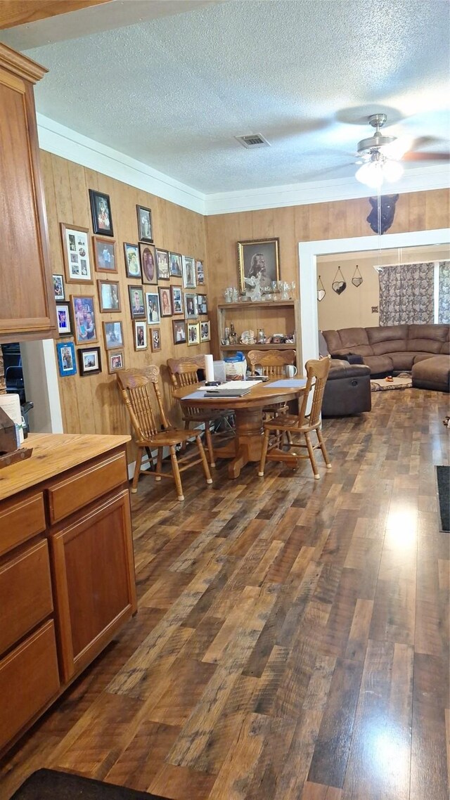 dining area featuring ceiling fan, dark hardwood / wood-style floors, wooden walls, and a textured ceiling