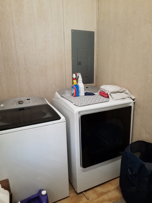 laundry area featuring electric panel, light wood-type flooring, wooden walls, and washing machine and dryer